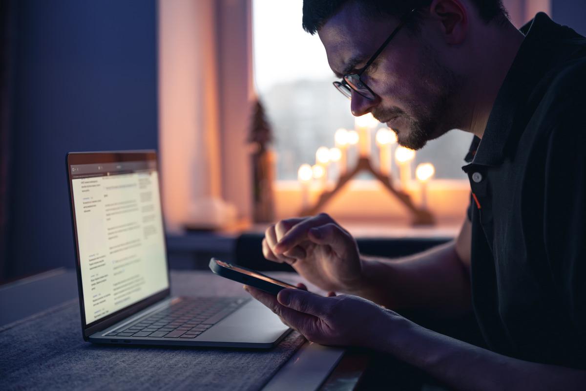 man-with-smartphone-sits-front-laptop-late-night